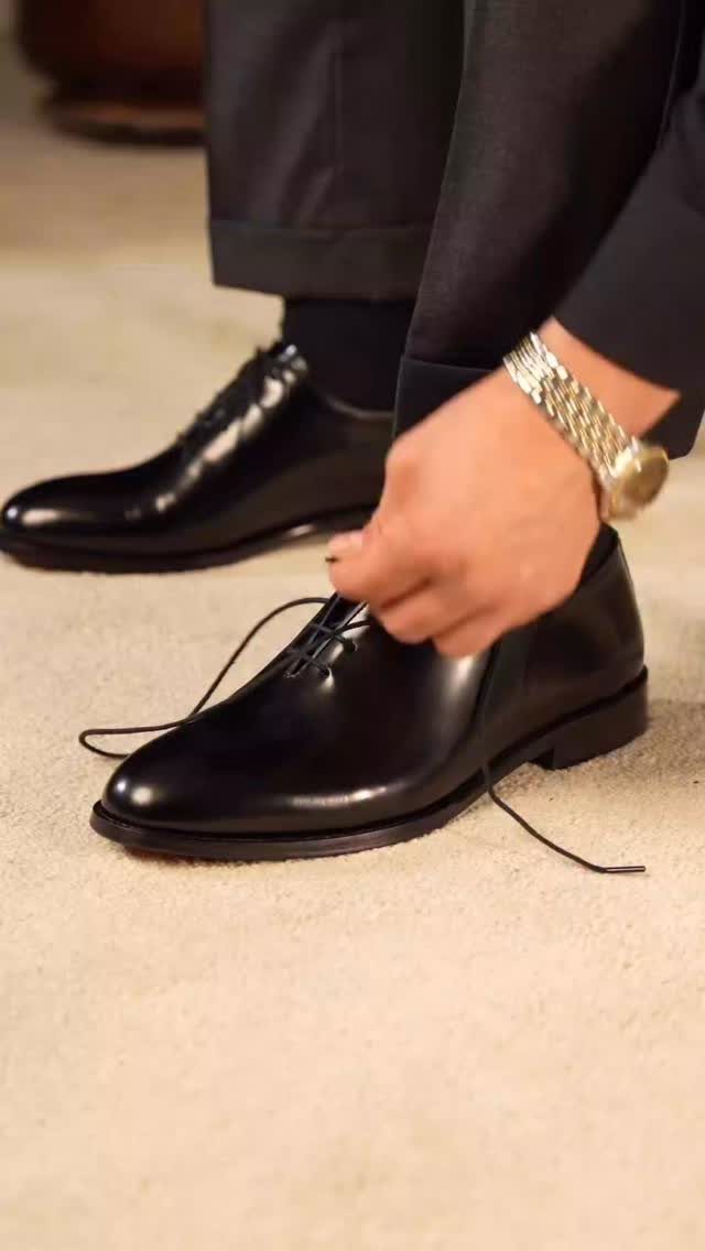 Black leather Oxford shoes being laced by a person wearing formal trousers.