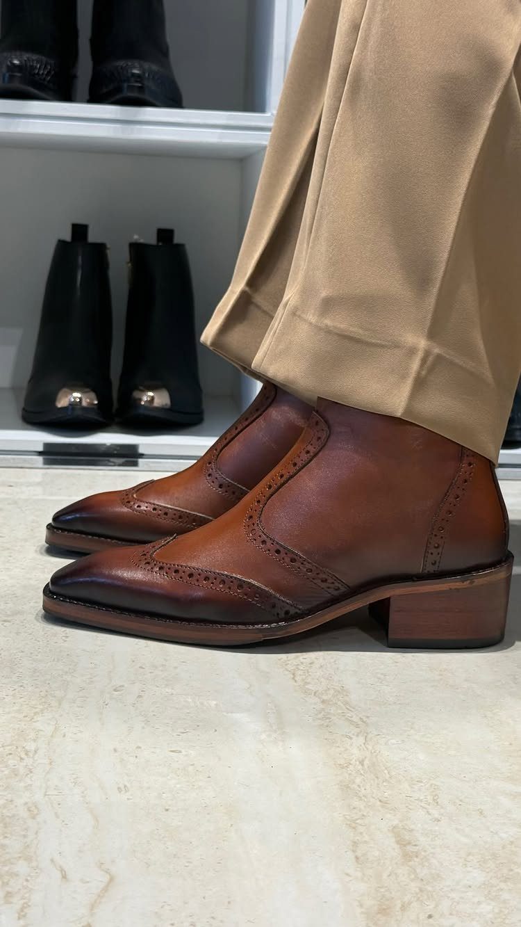 Brown leather wingtip ankle boots worn with tan trousers on marble flooring