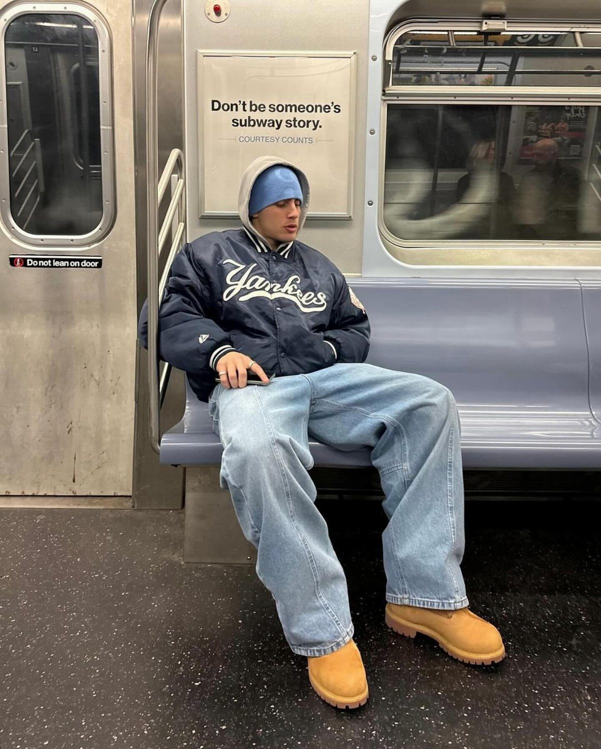 Person in a Yankees bomber jacket and wide-leg jeans wearing tan sheepskin boots.