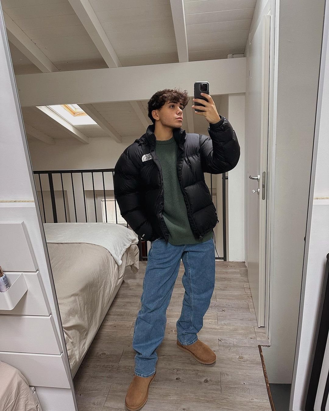 Person in black puffer jacket, blue jeans, and tan sheepskin boots taking mirror selfie