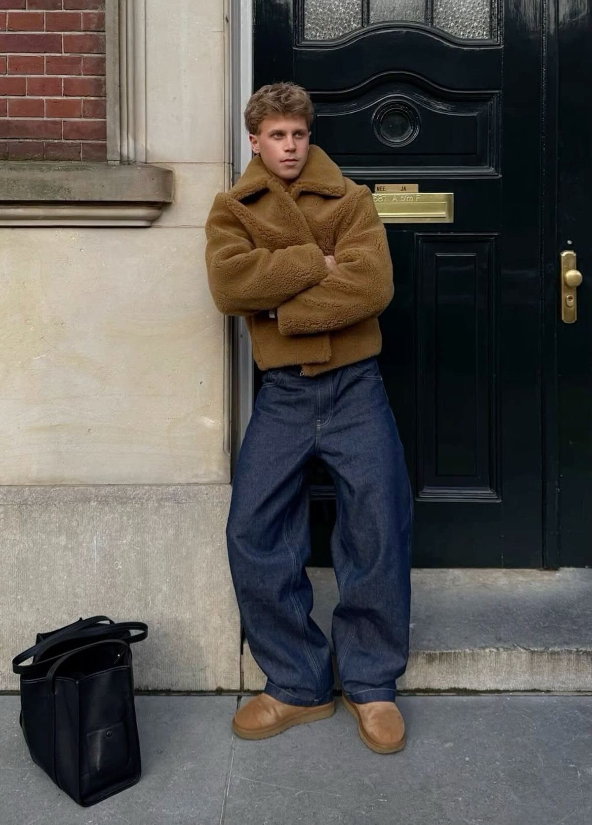 Man wearing brown fleece jacket, wide-leg blue jeans, and tan suede slip-on shoes.