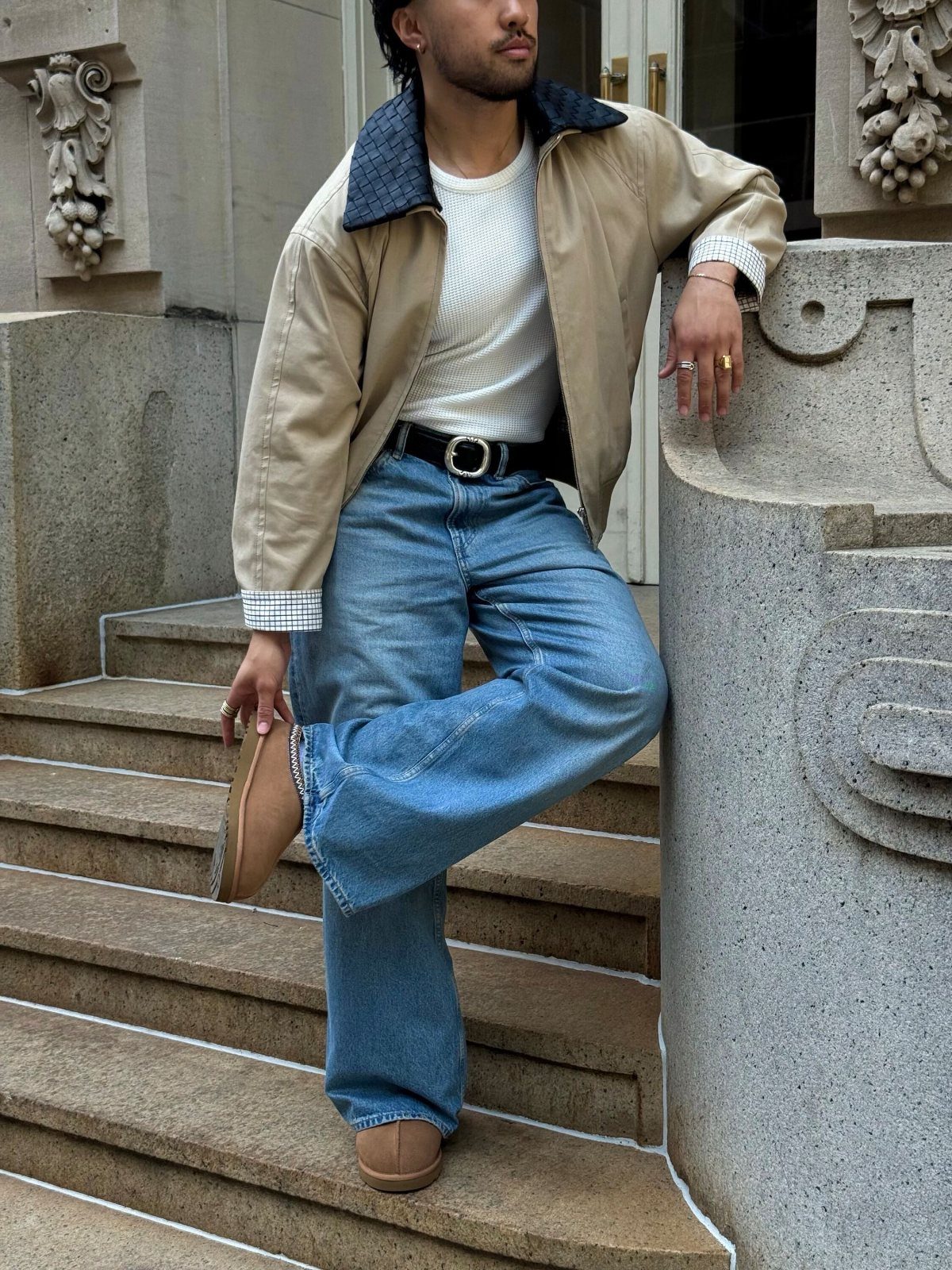 Man in tan jacket and blue jeans wearing tan suede slippers on stone steps