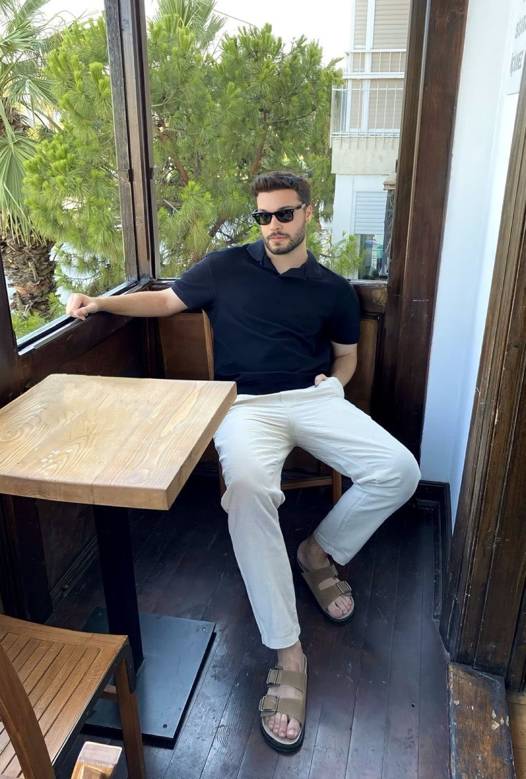 Man in black polo shirt and white chinos wearing tan double-strap slides.