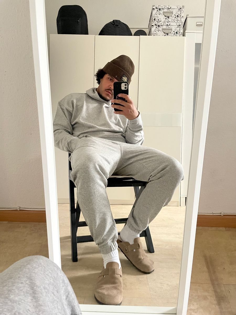 Man in grey hoodie and sweatpants wearing tan suede slides and brown beanie.