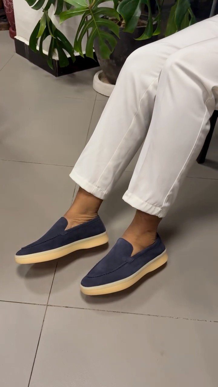 Navy blue slip-on loafers with cream soles paired with white trousers.