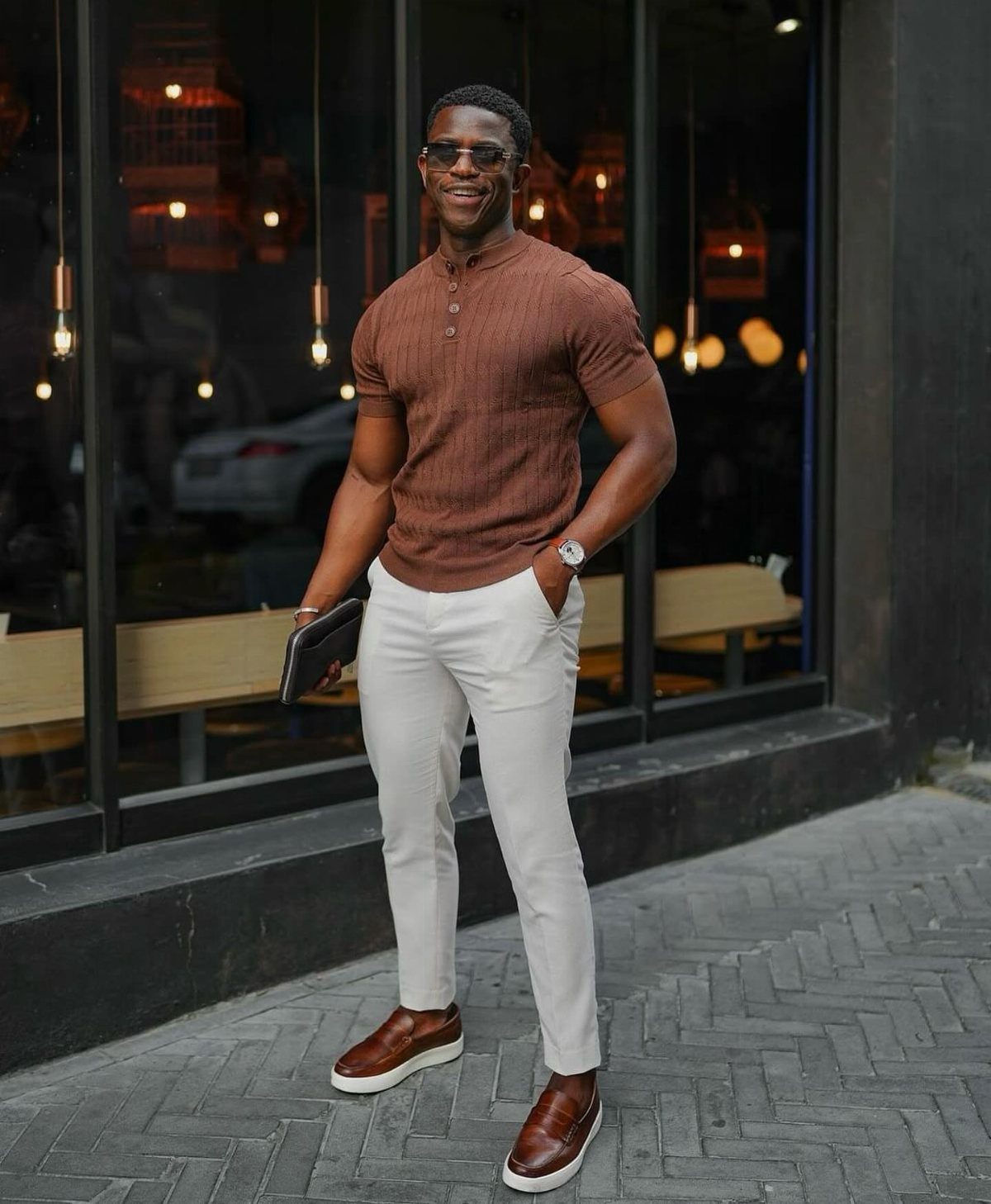 Man wearing brown henley shirt, white trousers, and brown leather shoes on sidewalk