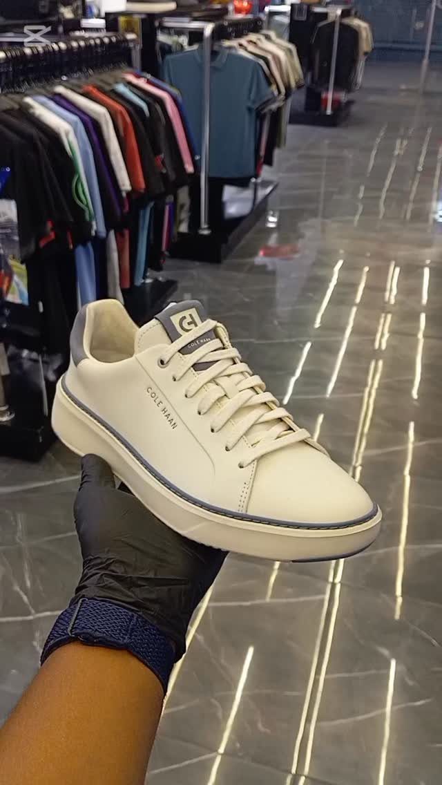 White Cole Haan sneaker held by a gloved hand in a clothing store.