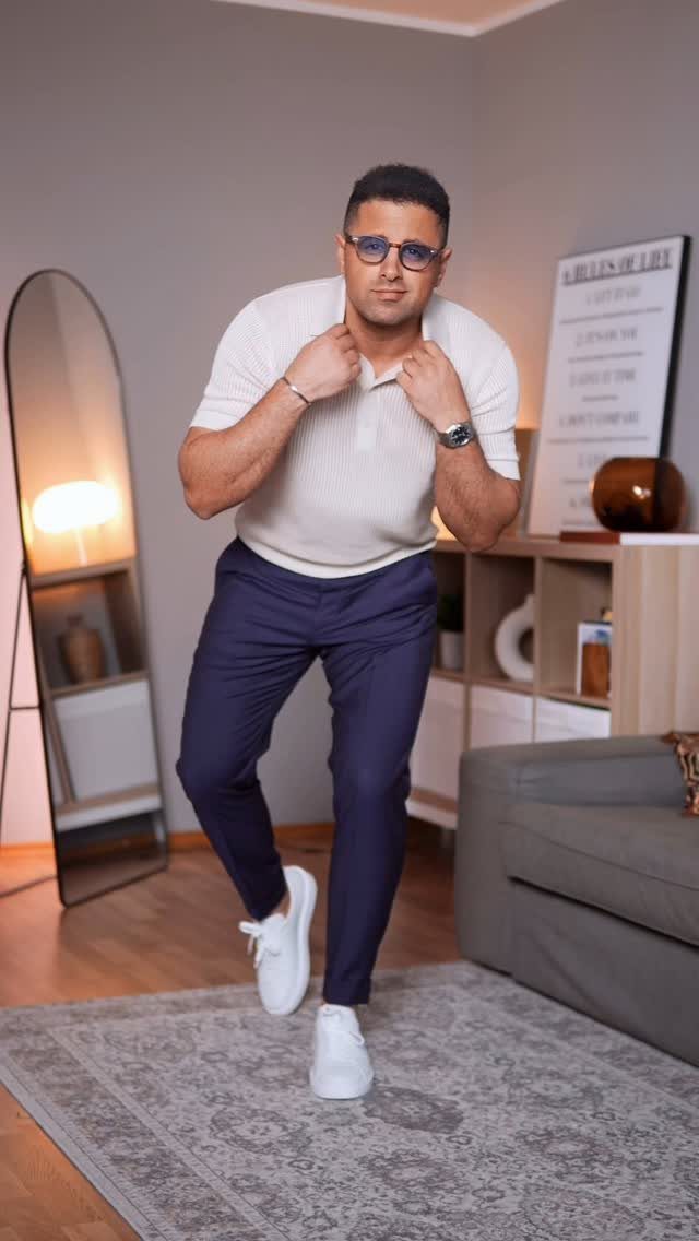 Man wearing white sneakers and navy blue dress pants in a modern living room.