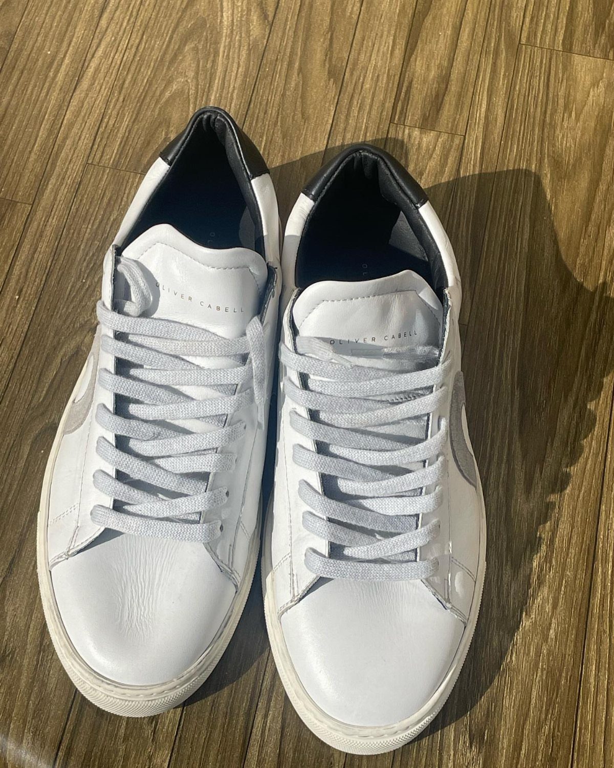 White leather dress sneakers with dark blue accents on a wooden floor