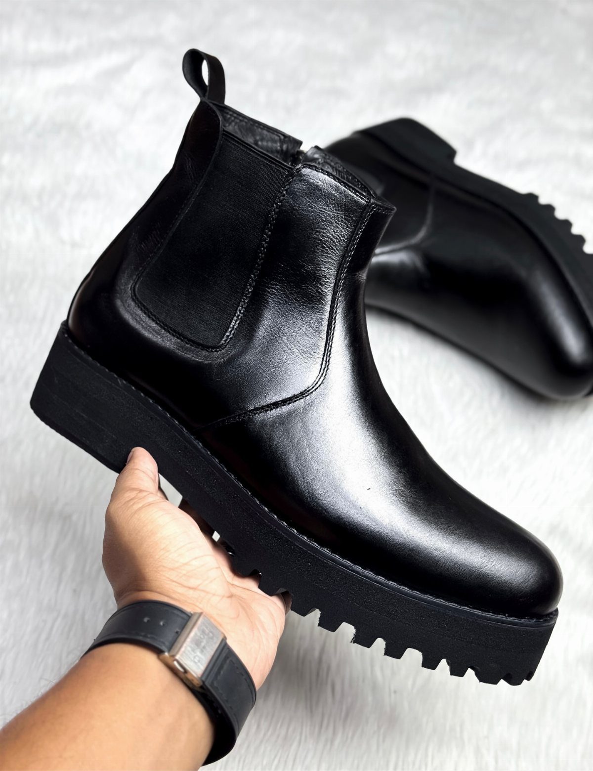 Black leather Chelsea boots with chunky lug soles held against a white background
