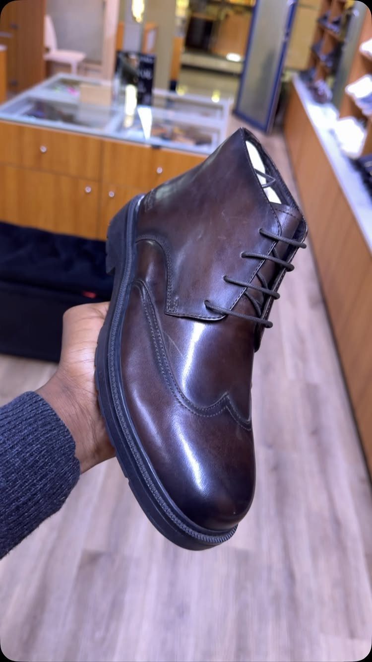 Dark brown leather lace-up boot held by a hand in a shoe store.