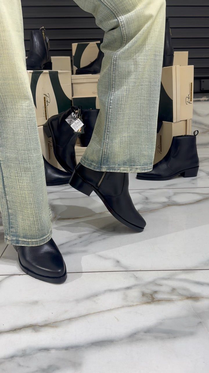 Black leather ankle boots with zippers worn with light textured trousers on marble floor.