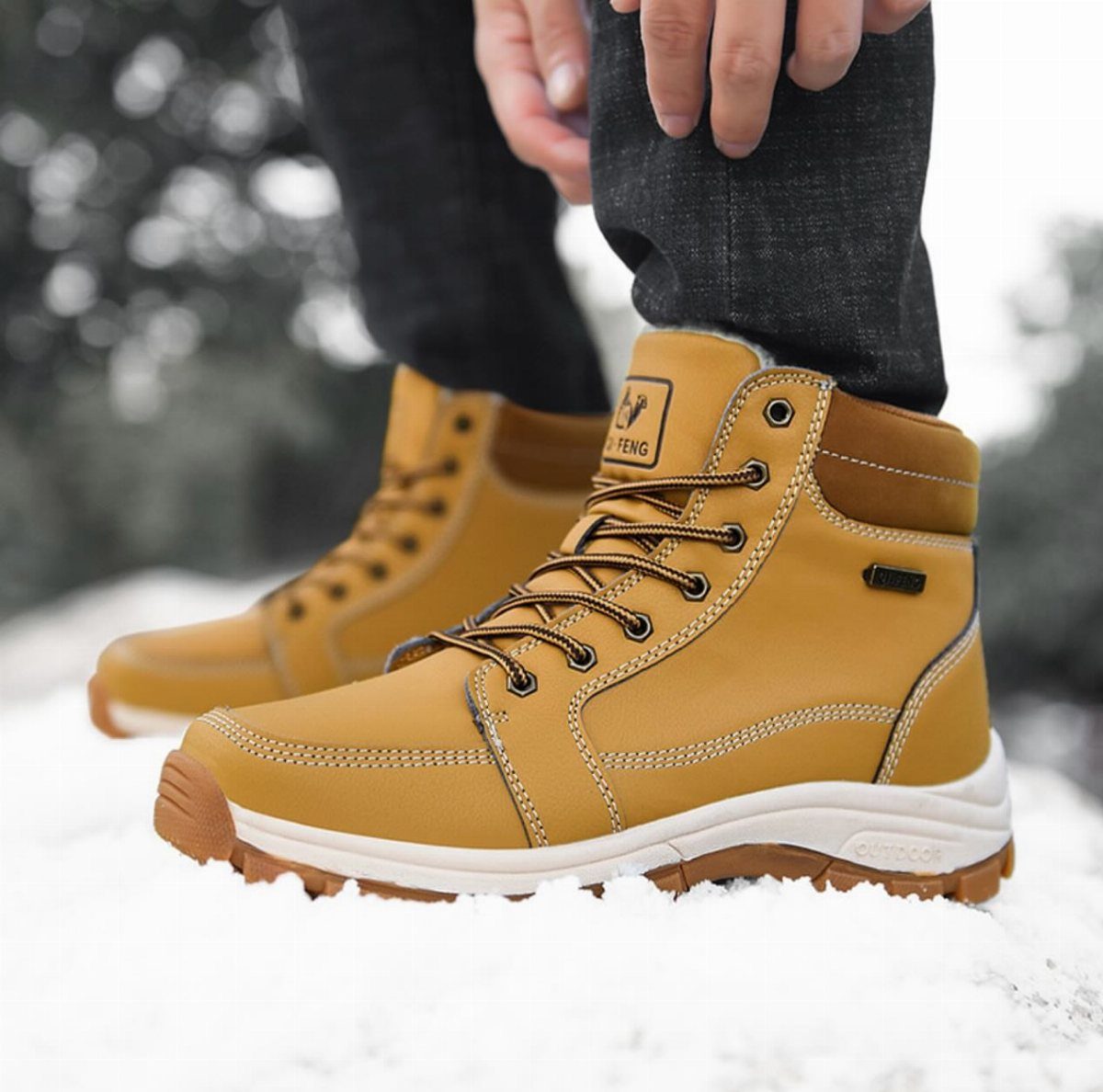 Tan insulated snow boots with white soles standing in fresh white snow