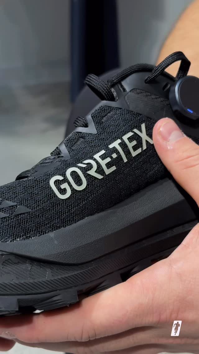 Black GORE-TEX trail running shoe held by a person's hands.