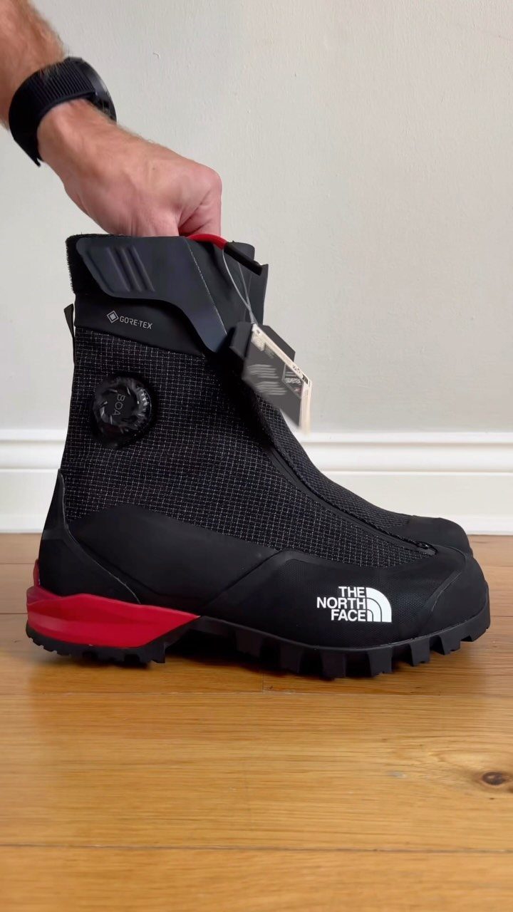 Black The North Face winter boot with red sole on a wooden floor