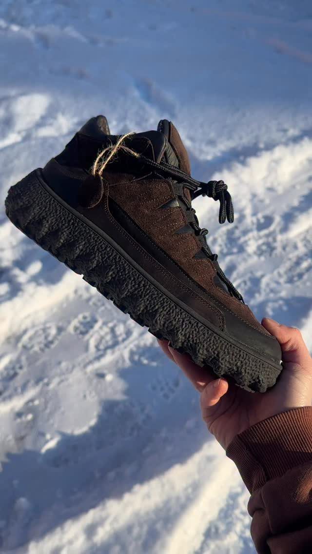Brown suede winter boot with thick black sole held over snowy ground.