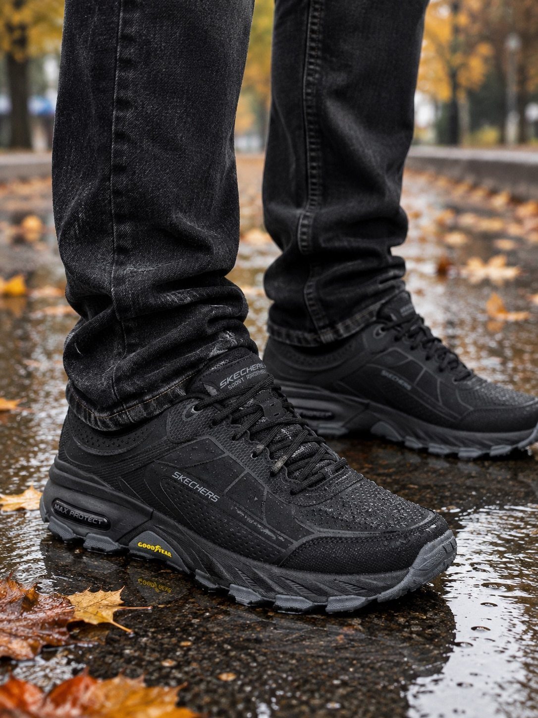 Black waterproof sneakers on a person standing on wet ground with autumn leaves.
